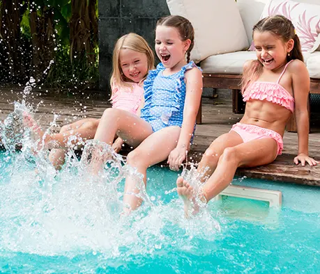 Three happy children splashing in a luxury backyard swimming pool with outdoor patio seating