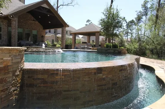 Luxury custom pool with curved stone walls and integrated spa in upscale backyard entertainment area