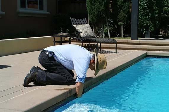 Pool contractor inspecting and maintaining luxury backyard swimming pool edge