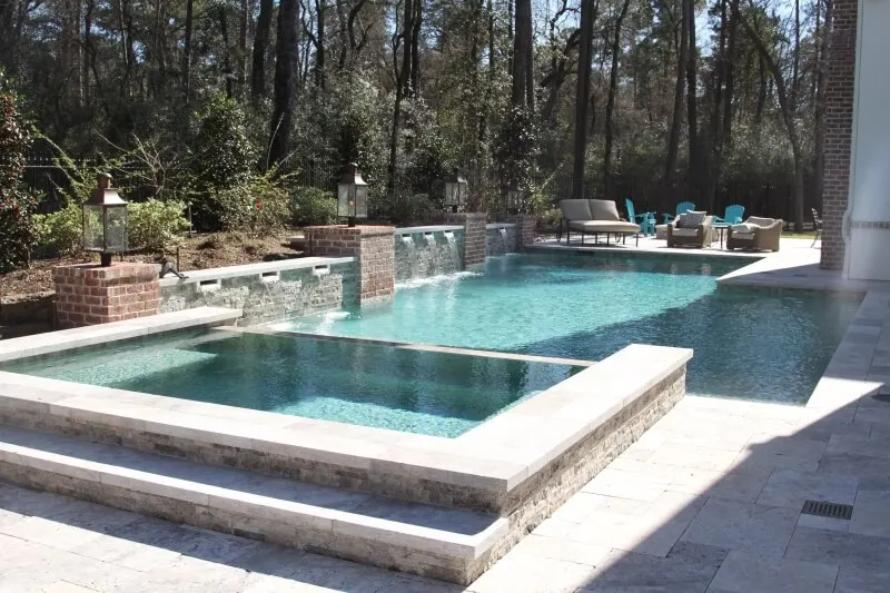 Luxury backyard pool with geometric design, spa, and sheer descent water features surrounded by stacked stone