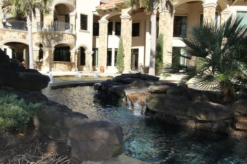 Luxury backyard pool with natural stone waterfall and spa in Mediterranean-style courtyard setting