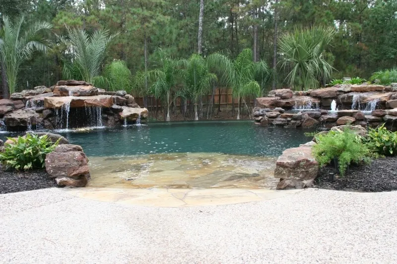 Luxury backyard pool with natural beach entry, rock waterfall, and spa surrounded by tropical landscaping