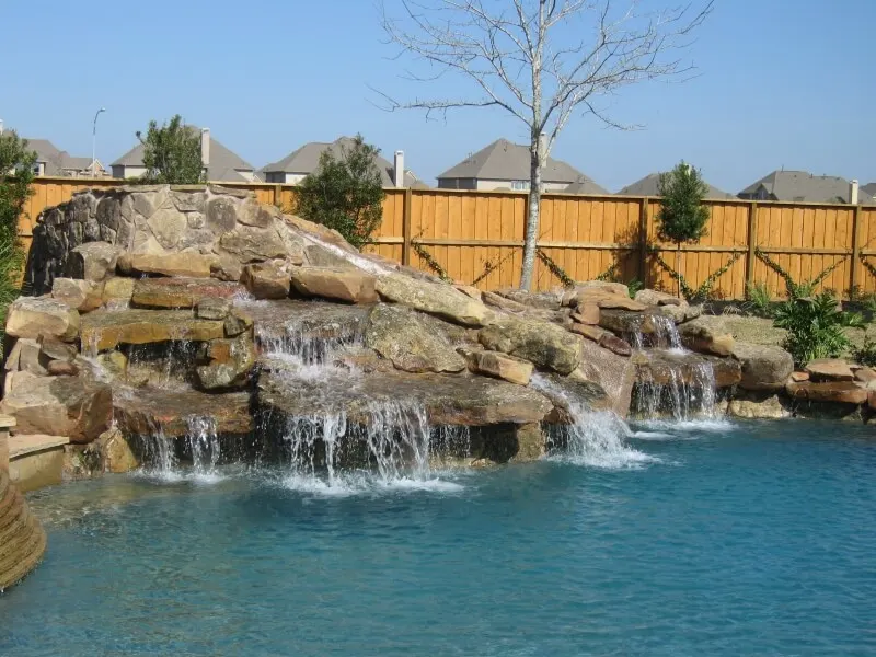 Luxury backyard pool with rock waterfall feature and turquoise water in residential setting