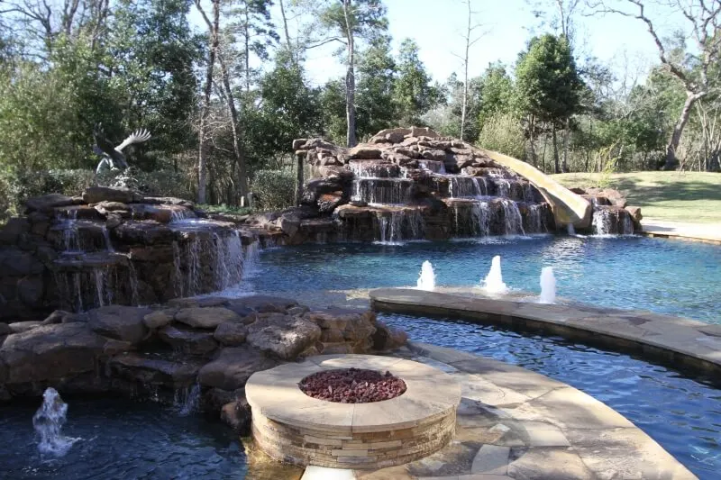 Luxury backyard pool with waterfall, lazy river, fire pit, and bubblers surrounded by trees