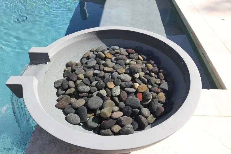 Water bowl water feature filled with smooth river stones in luxury backyard pool design